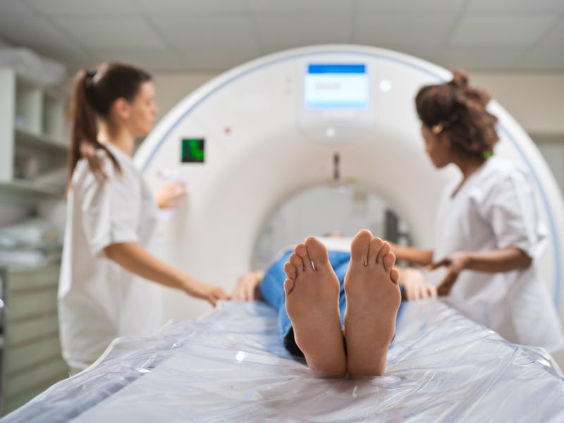 Female doctors assisting male patient while doing MRI scan in medical examination room. Focus on pat...