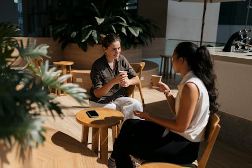 Two friends indulge in a lively conversation over refreshing coffee at modern cafe. Young women sitt...