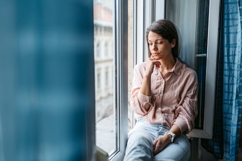 Depressed young woman sitting by the window and contemplating life in Budapest in Hungary.