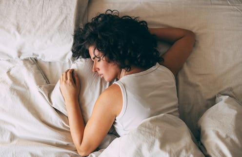 A woman with curly hair peacefully sleeping in a cozy bed, showcasing relaxation and restfulness. Pe...