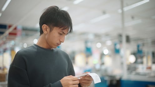 Asian man shocked while looking at bill after shopping in the mall.