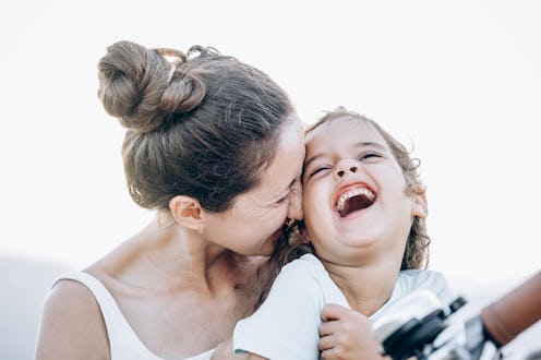 Close-up happy portrait of mother and her little laughing daughter on a walk. Joyful mother kisses h...