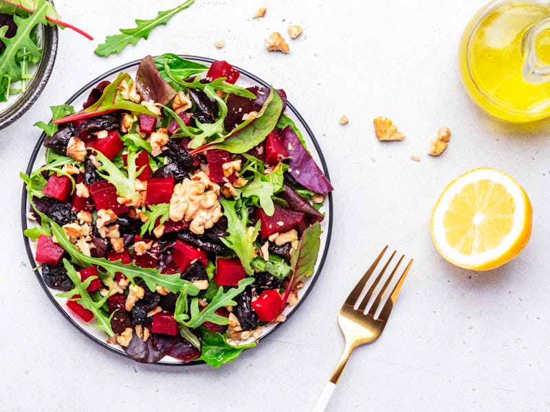 Beet and herbs healthy salad with prunes, arugula, chard and walnuts, gray table. Fresh useful vegan...