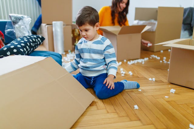 Toddler looking at a cardboard box, mother packing in background for house move. Moving during child...