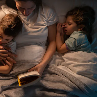 Young mother reading stories to her kids before speeping while they lying in bed