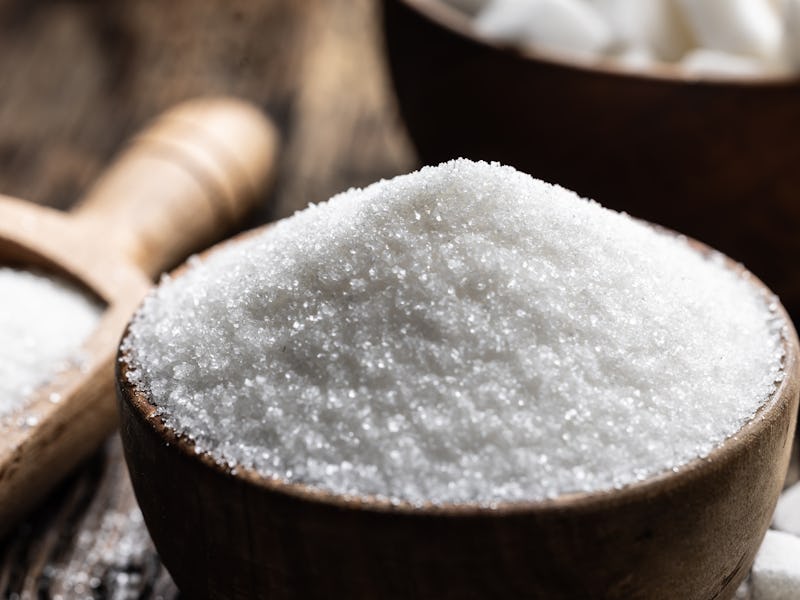 Granulated sugar in a wooden scoop or bowl on an old oak table.