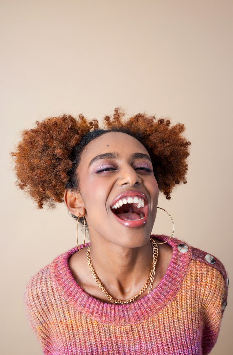Portrait of excited gen z black young woman wearing colorful pink sweater laughing at camera with ey...