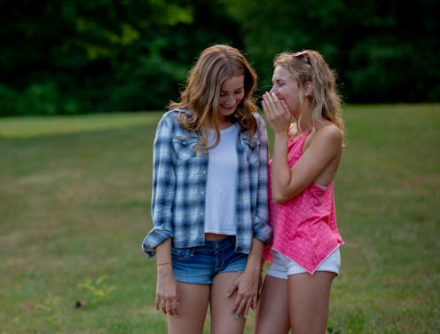 Two teenage girls are seen walking together outside as they whisper and tell secrets to one another....