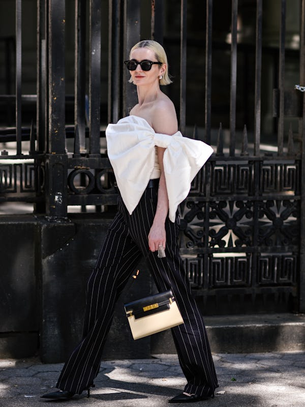 NEW YORK, NEW YORK - SEPTEMBER 11: A guest is seen wearing a white bow top, black pinstripe pants an…
