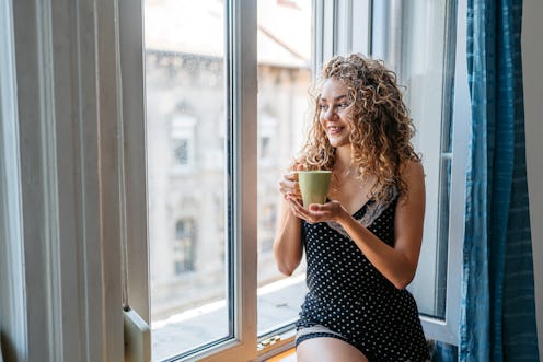 Beautiful young woman drinking coffee by the window in the morning in Budapest in Hungary.