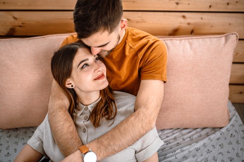Young smiling couple embracing in bedroom, looking to each other full of love.