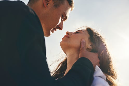 A couple stands close together, the man holding the woman’s face gently. Both are looking into each ...