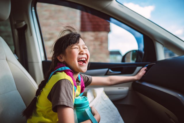 Young cheerful girl in her Girl Guide’s uniform, laughing joyfully while sitting in the passenger se...