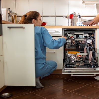 Mother and her teenage daughter unloading clean plates from dishwasher.
