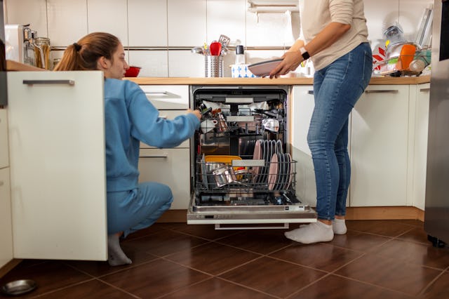 Mother and her teenage daughter unloading clean plates from dishwasher.