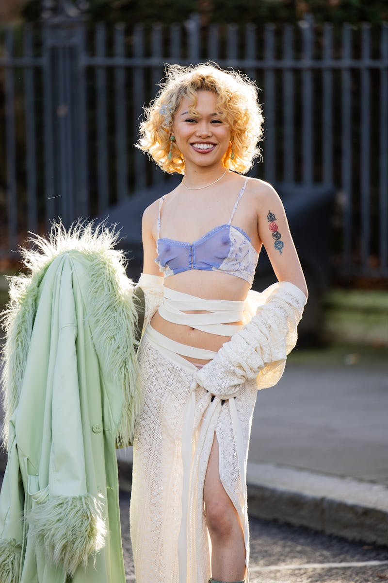 LONDON, ENGLAND - FEBRUARY 18: Jessie-Mae Alonzo wears cut out skirt, cropped purple top, green coat…