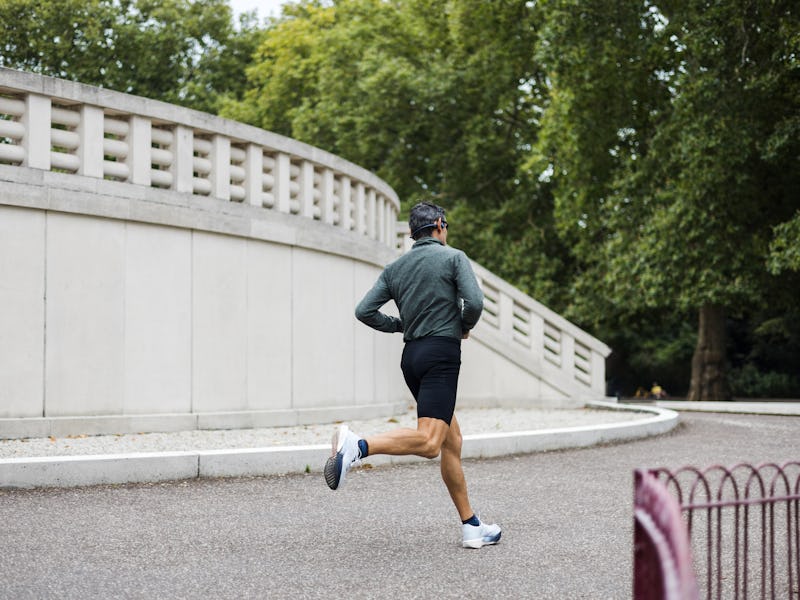 A man runs on a sidewalk in front of a building. The man is wearing a black shirt and shorts