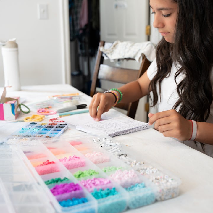 A girl sits at her kitchen table making bracelets, in a story about dopamine menus for kids and fami...