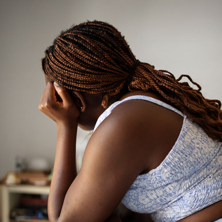 Young teenage girl looking upset after checking her smart phone while sitting alone on her bed at ho...