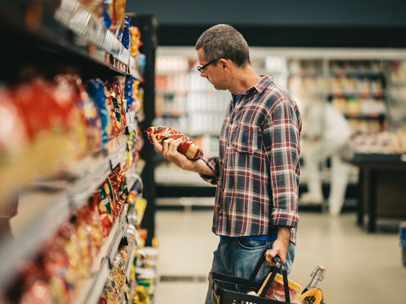 Man standing in a supermarket aisle and reading the label on a bag of pasta while grocery shopping
