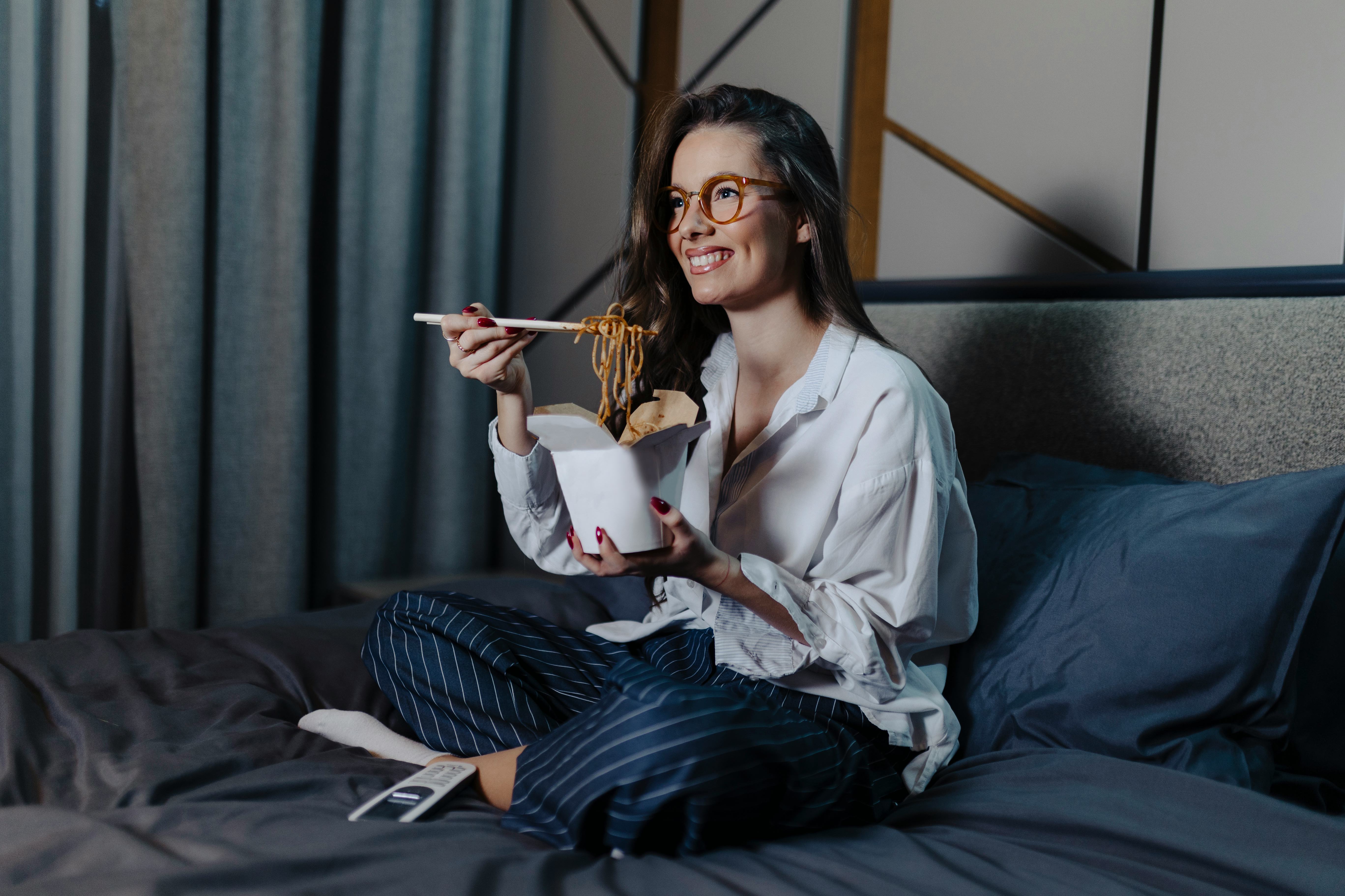 Woman eating pasta and watching movie at bed at night