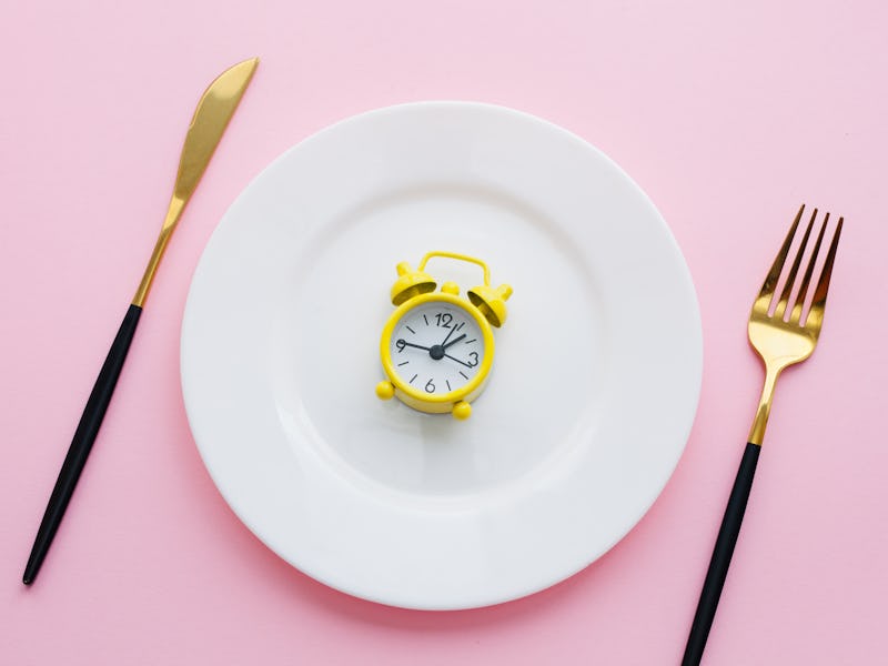 White plate with pink glitter confetti, golden and black fork and knife, yellow alarm clock over pin...