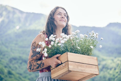 A woman with a box of seedlings of white cornflowers on the background of mountains.