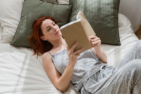 Young woman is lying in bed reading a book, enjoying a quiet moment at home