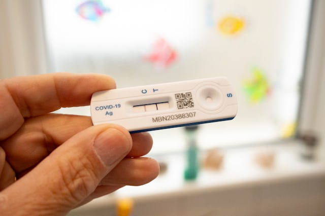 A detail of a hand holding a Covid lateral flow test that shows a positive result in a bathroom — yo...