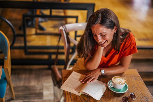 young woman is sitting in a cafe and enjoying her coffee. young woman read book