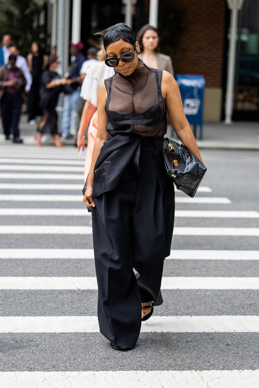 NEW YORK, NEW YORK - SEPTEMBER 07: A guest wears black transparent top, high waisted pants, bag outs...