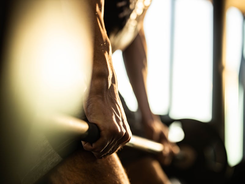 Close up of unrecognizable athletic man exercising strength with barbell in a gym.
