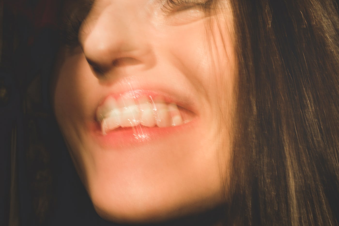Happy woman: closeup of woman's face and mouth smiling. The candid woman's mouth is open with happiness and laughter. Woman could also appear to be talking, laughing, or flirting. There is motion blur and movement. Part of a series.