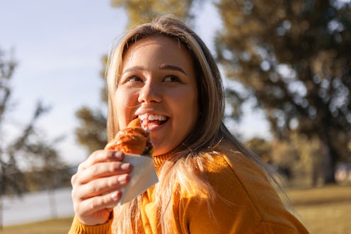 Woman eating croissant sandwich by the river in the morning