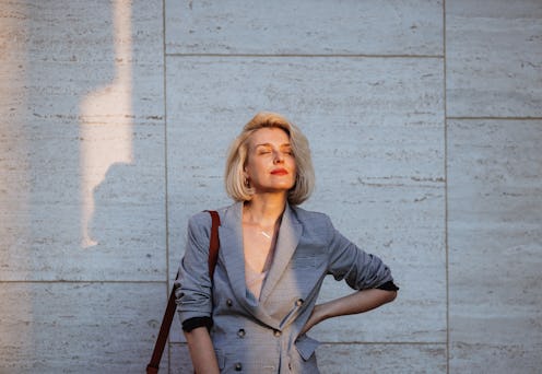 A confident woman in a stylish business outfit enjoys the urban environment. She stands with one han...