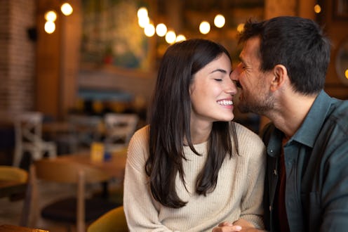 Close-up of a loving couple sitting in a cafeteria. A handsome man kissing his girlfriend on the che...