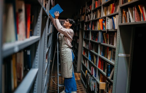 Young beautiful librarian reorganizing books in her library