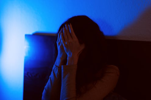 A moody and evocative image of a person covering their face in distress, captured in low light with ...
