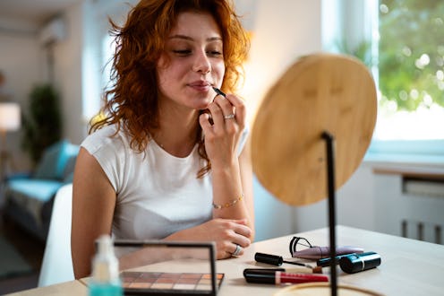 Redhead Caucasian teenage girl looking at herself in the small mirror, while applying lip liner