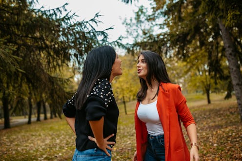 Two young female friends arguing in a public park during autumn.