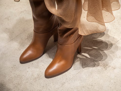 A stylish pair of brown leather boots with a smooth, polished finish, complemented by a flowing, she...