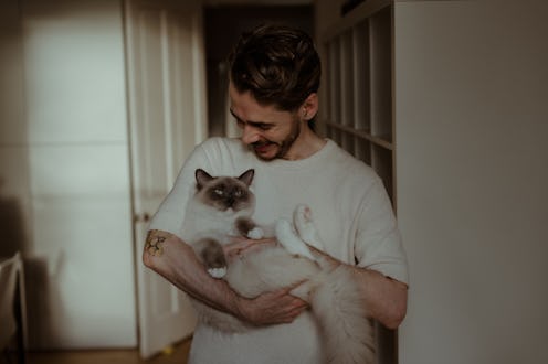 A smiling man is holding a Ragdoll cat, which is lying on its back and looking relaxed. The image ca...