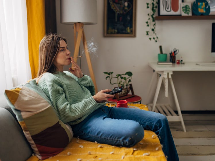 Beautiful woman relaxes at home, watching TV, smoking a joint and enjoying her day off
