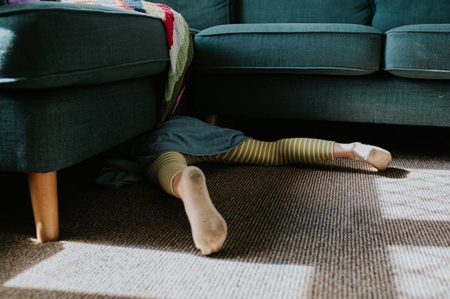 Conceptual image of a little girl crawling under a corner sofa. We can see the soles of her feet, an...