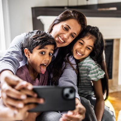 Mother and two children taking a selfie with smartphone; the child in the foreground makes a silly face.