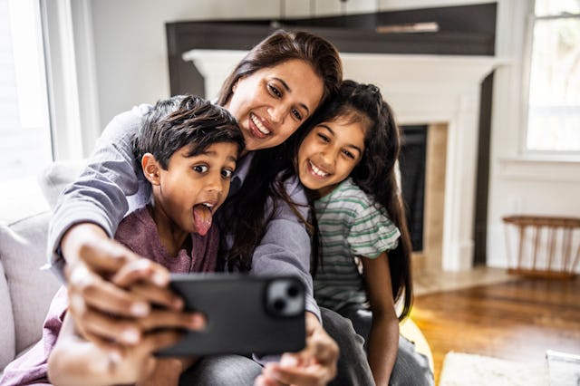 Mother and two children taking a selfie with smartphone; the child in the foreground makes a silly f...