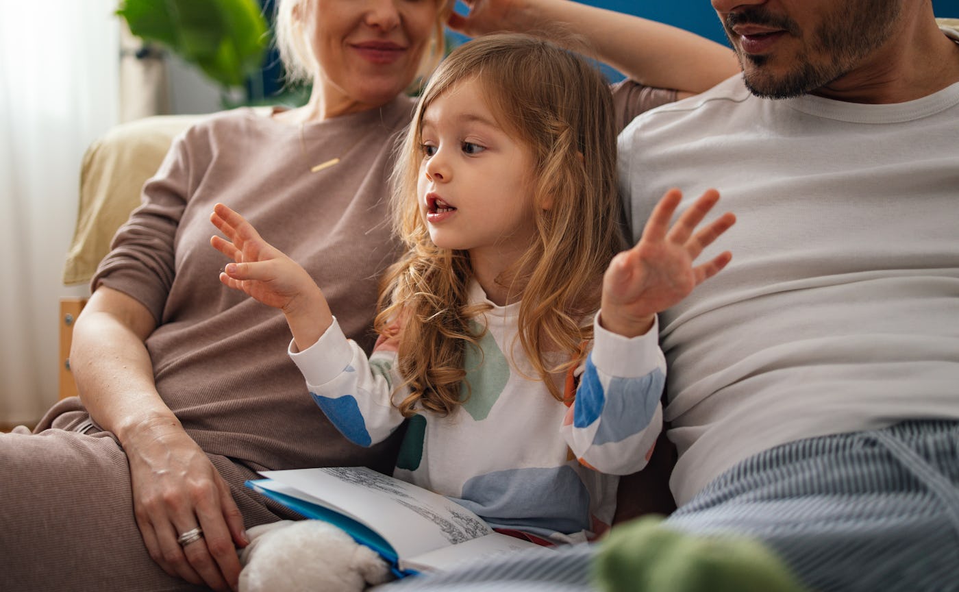 Close up photo of a smiling daughter explaining a fairy tale to her mother and unrecognizable father at home.