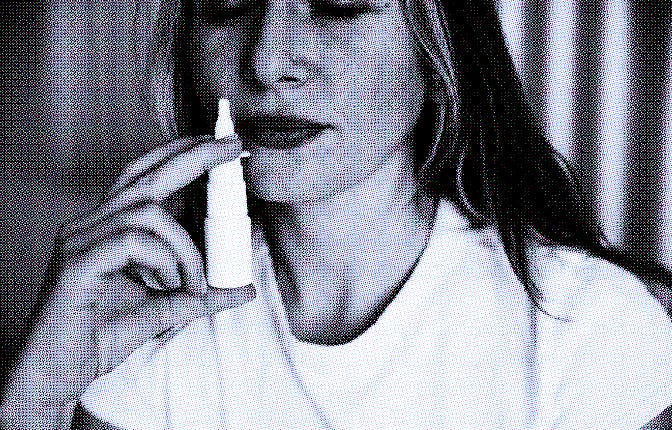 Caucasian woman is shown using a nasal spray in her bedroom to alleviate her congestion. Treatment f...