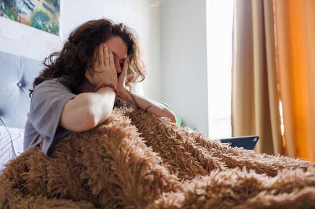 Mental burnout. Caucasian brunette woman can't wake up in the morning, sit with head in hands in bed