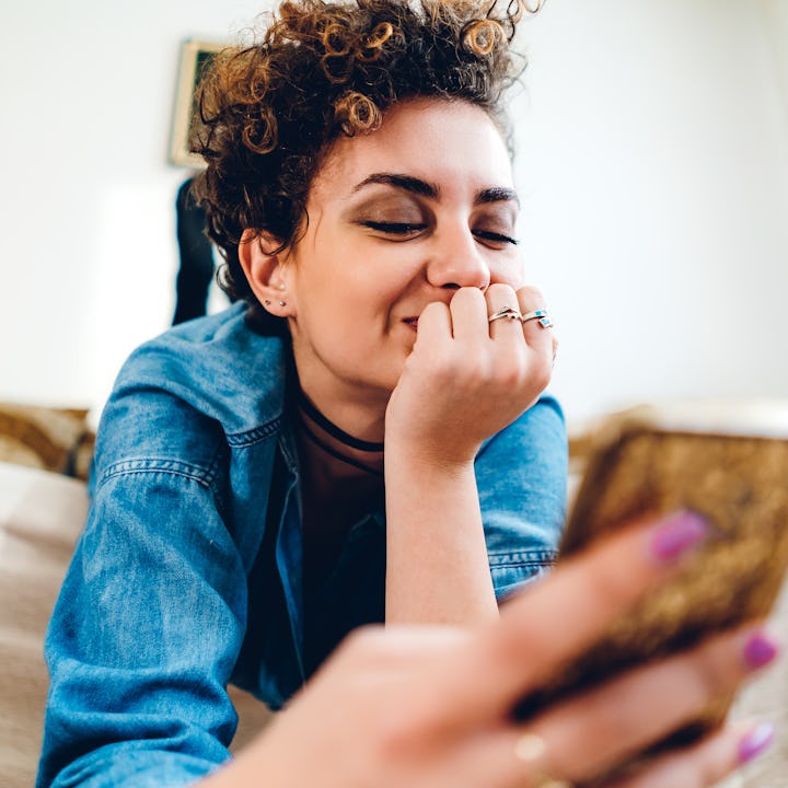 Young woman, with short, curly hair, using phone, in her apartment, lying upside down.